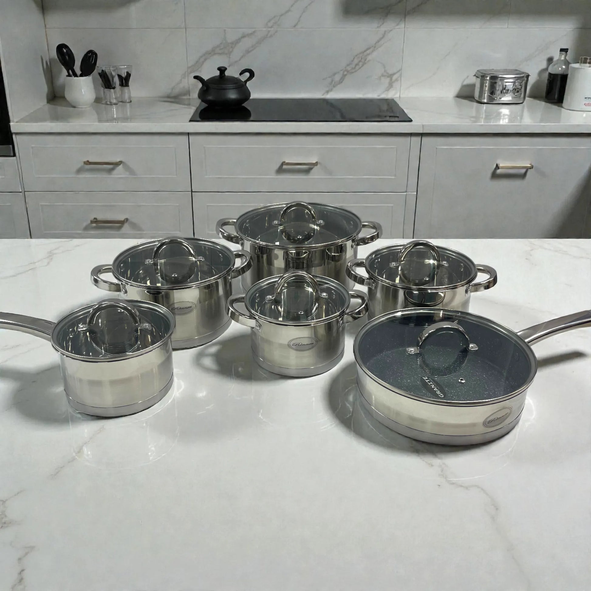 Set de ollas Rönner Austria de 12 piezas en acero inoxidable sobre top de mármol en cocina moderna.