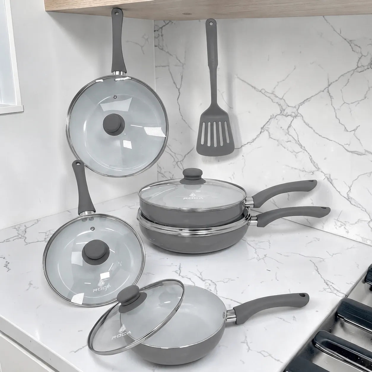 Set de sartenes ROCA color gris apilados con tapas de vidrio, mangos ergonómicos grises y espátula incluida, modelo KFS5000N.