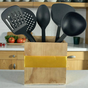 Utensilios de cocina JiaHang negros con mango de acero inoxidable (set 5 piezas, 32 cm) colocados en un porta-utensilios de madera; se ven al frente espátula ranurada, espumadera, cuchara, espátula sólida y cucharón en cocina.