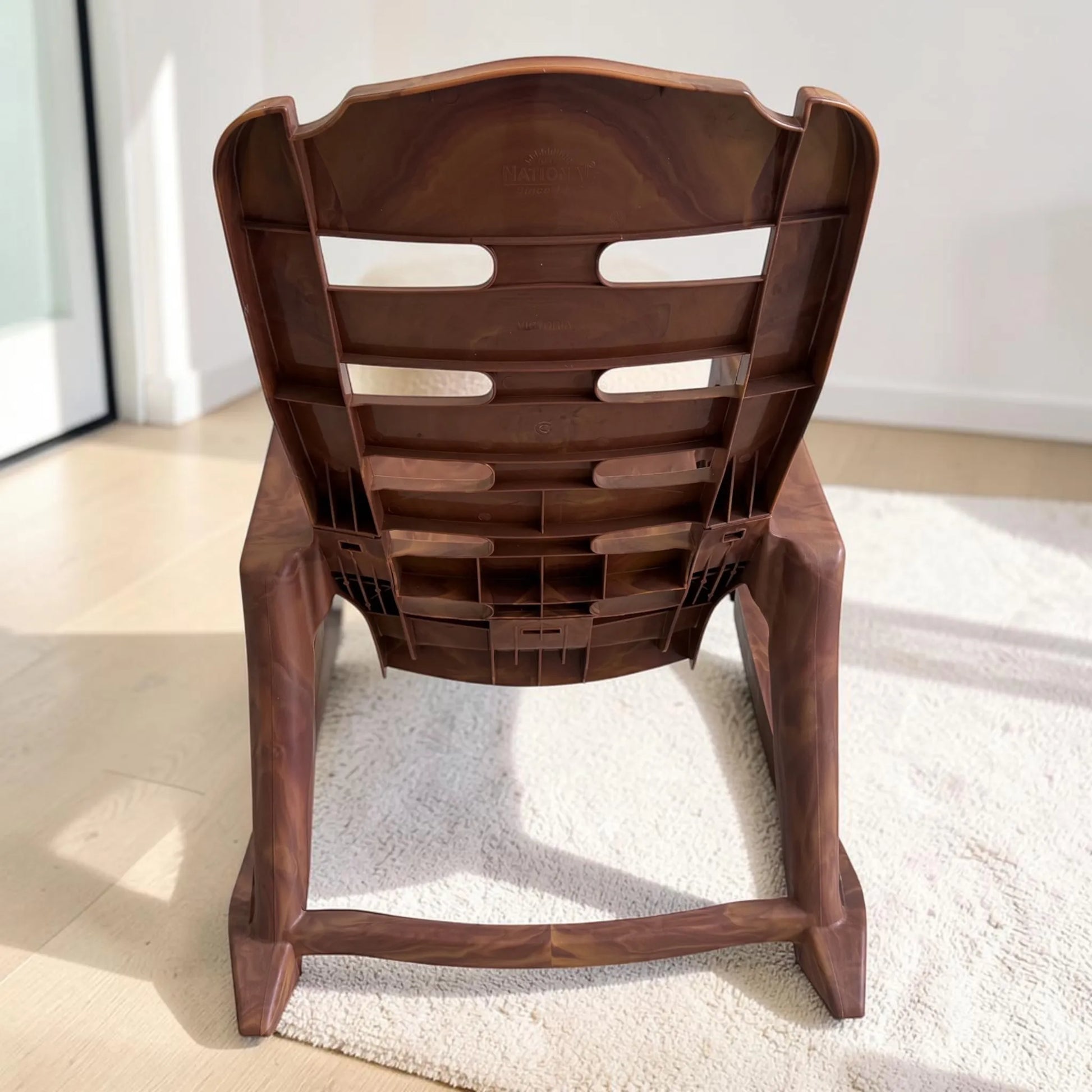 Parte trasera de silla mecedora plástica National acabado Mango, con respaldo alto ventilado y estructura plástica reforzada.