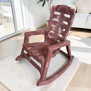 Silla mecedora plástica National acabado Sándalo, vista frontal lateral, con respaldo alto ventilado, brazos integrados y base curva de balanceo.