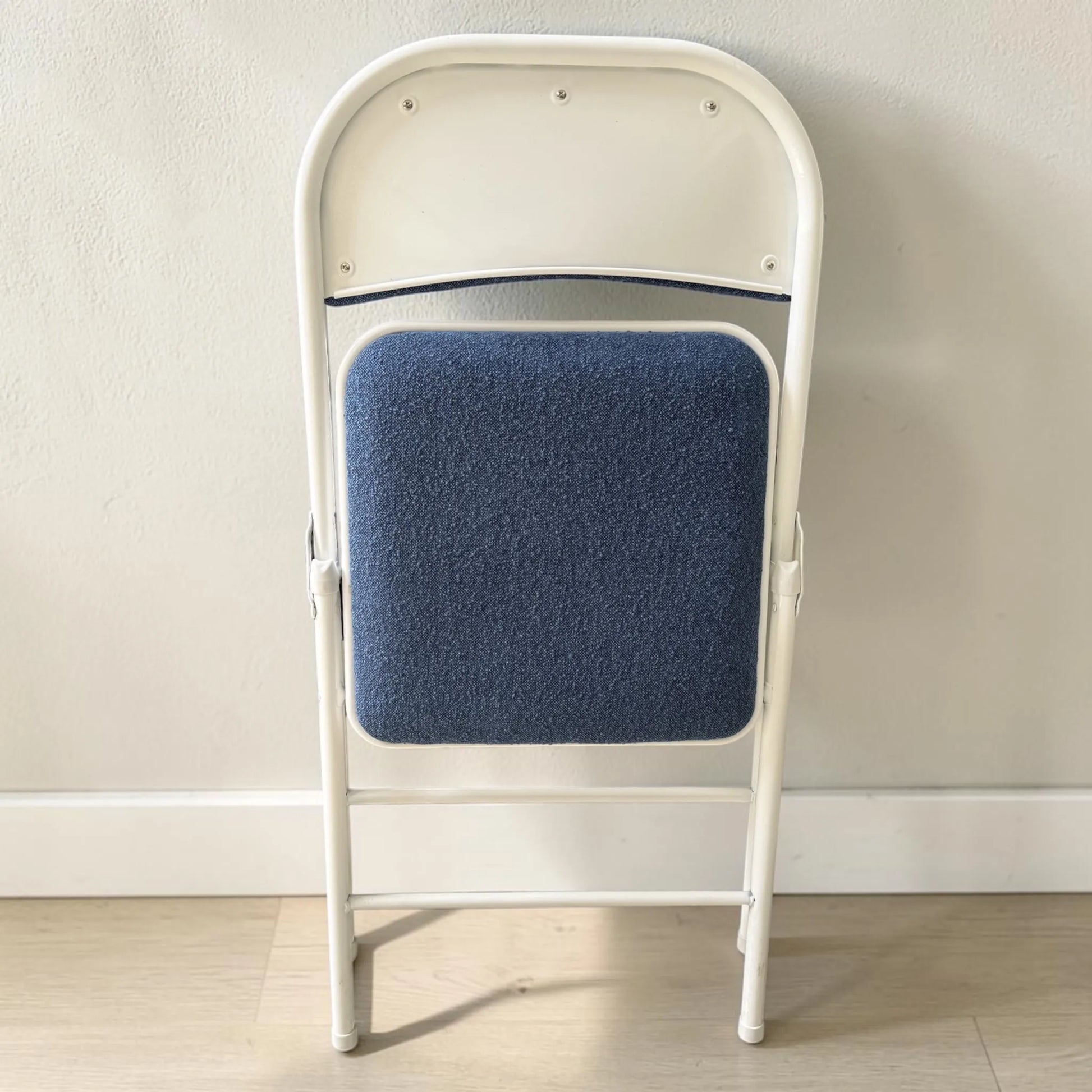 Silla plegable azul CH-3023-BLU en posición plegada con estructura blanca, ideal para ahorrar espacio.