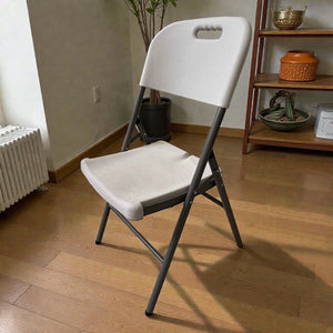 Silla plegable Lotus color blanco con estructura metálica gris oscuro, vista angular frontal 3/4, silla abierta para interior, medidas 46 × 54 × 86 cm.