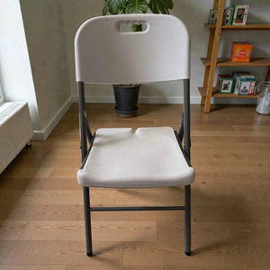 Vista frontal de silla plegable Lotus blanca con estructura metálica gris, asiento y respaldo de plástico texturizado, medidas 46 × 54 × 86 cm.