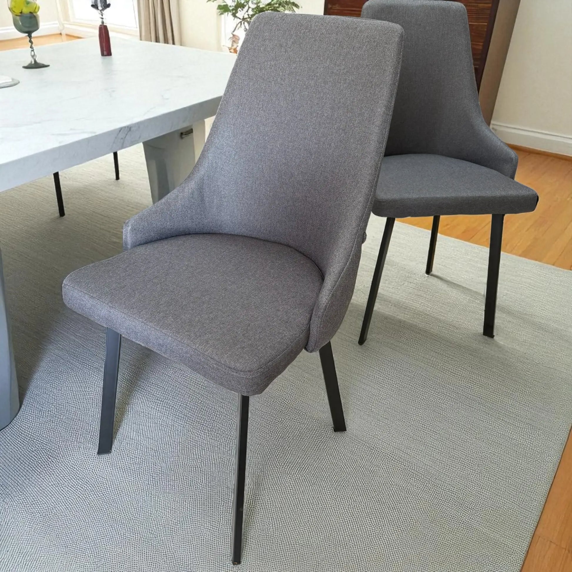 Par de sillas de comedor gris oscuro del set Ambienta DT-06-2237 junto a mesa rectangular 156×86×76 cm con cubierta tipo mármol blanco; ambiente moderno con piso de madera.