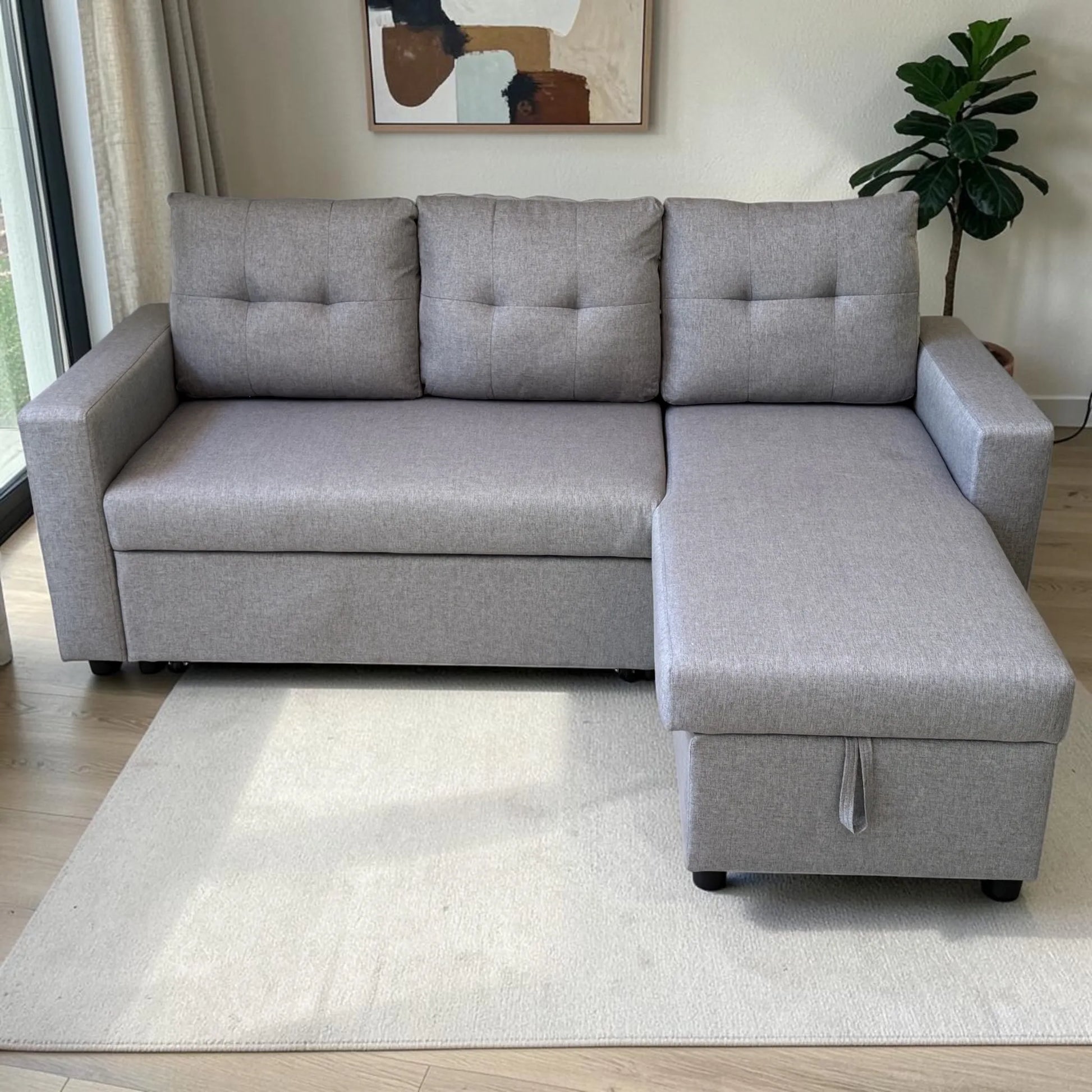 Sofá cama 2 en 1 Ambienta Home Decor color gris claro, vista frontal con chaise al lado derecho, tres respaldos acolchados, brazos rectos y tapizado tipo tela.