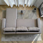 Vista superior del sofá cama 2 en 1 Ambienta Home Decor color gris claro con chaise longue, tres cojines removibles, brazos rectos y tapizado tipo lino en sala moderna.