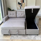 Sofá cama gris claro con cajón de almacenamiento abierto en chaise derecha, tapa levantada, interior negro amplio y mecanismo de bisagras visible.