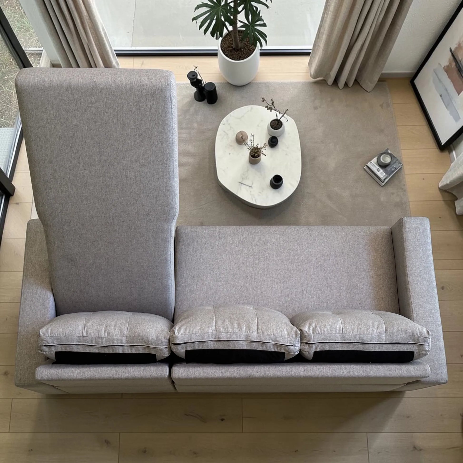 Sofá cama gris claro visto desde arriba, con cajón de almacenamiento abierto, tres cojines removibles, superficie extendida y diseño convertible.