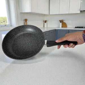 Sartén Stonewell 24 cm antiadherente con revestimiento tipo piedra negro/gris moteado, sostenido con la mano sobre encimera en cocina.