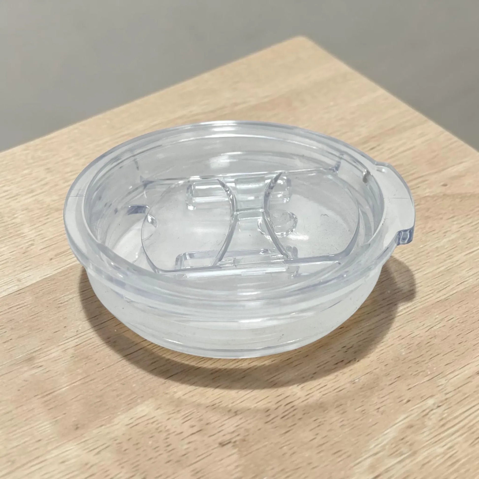 Tapa acrílica transparente removible para vaso térmico de 16 oz, vista lateral sobre mesa de madera.