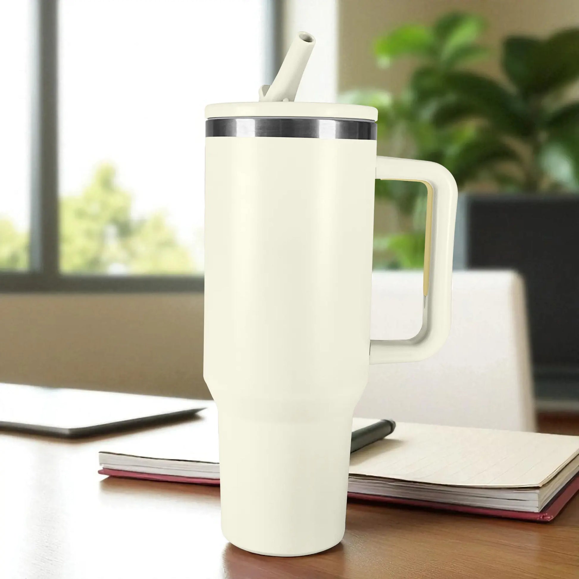 Termo blanco de acero inoxidable 1200 ml con asa y tapa de rosca con pajilla, colocado sobre escritorio junto a cuaderno.