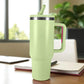 Termo verde claro de acero inoxidable 1200 ml con asa y tapa de rosca con pajilla, colocado sobre escritorio junto a cuaderno.