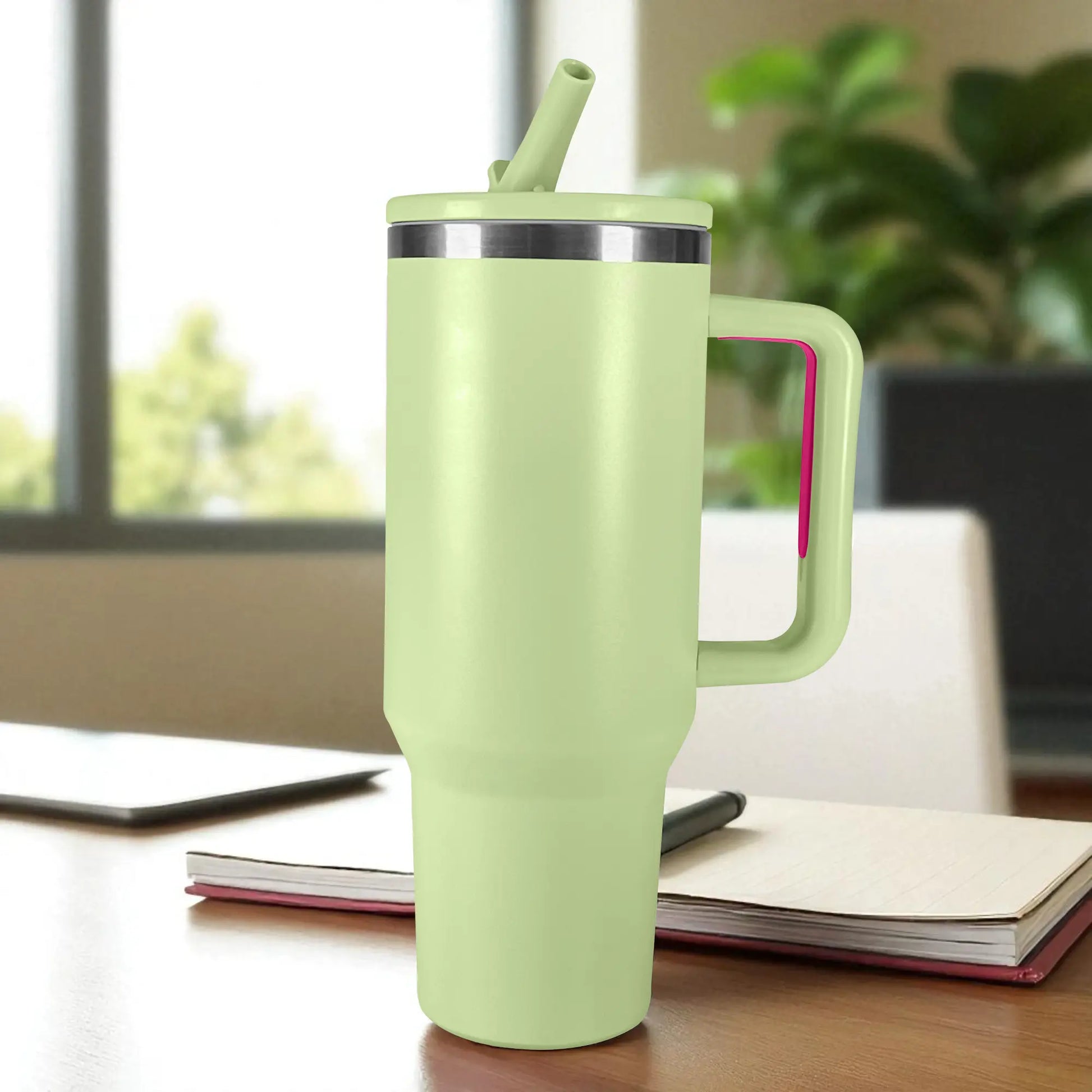 Termo verde claro de acero inoxidable 1200 ml con asa y tapa de rosca con pajilla, colocado sobre escritorio junto a cuaderno.