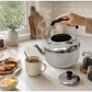 Tetera con silbato Lotus de 6 litros preparando té, con vapor, taza, limón y galletas en una cocina iluminada naturalmente.