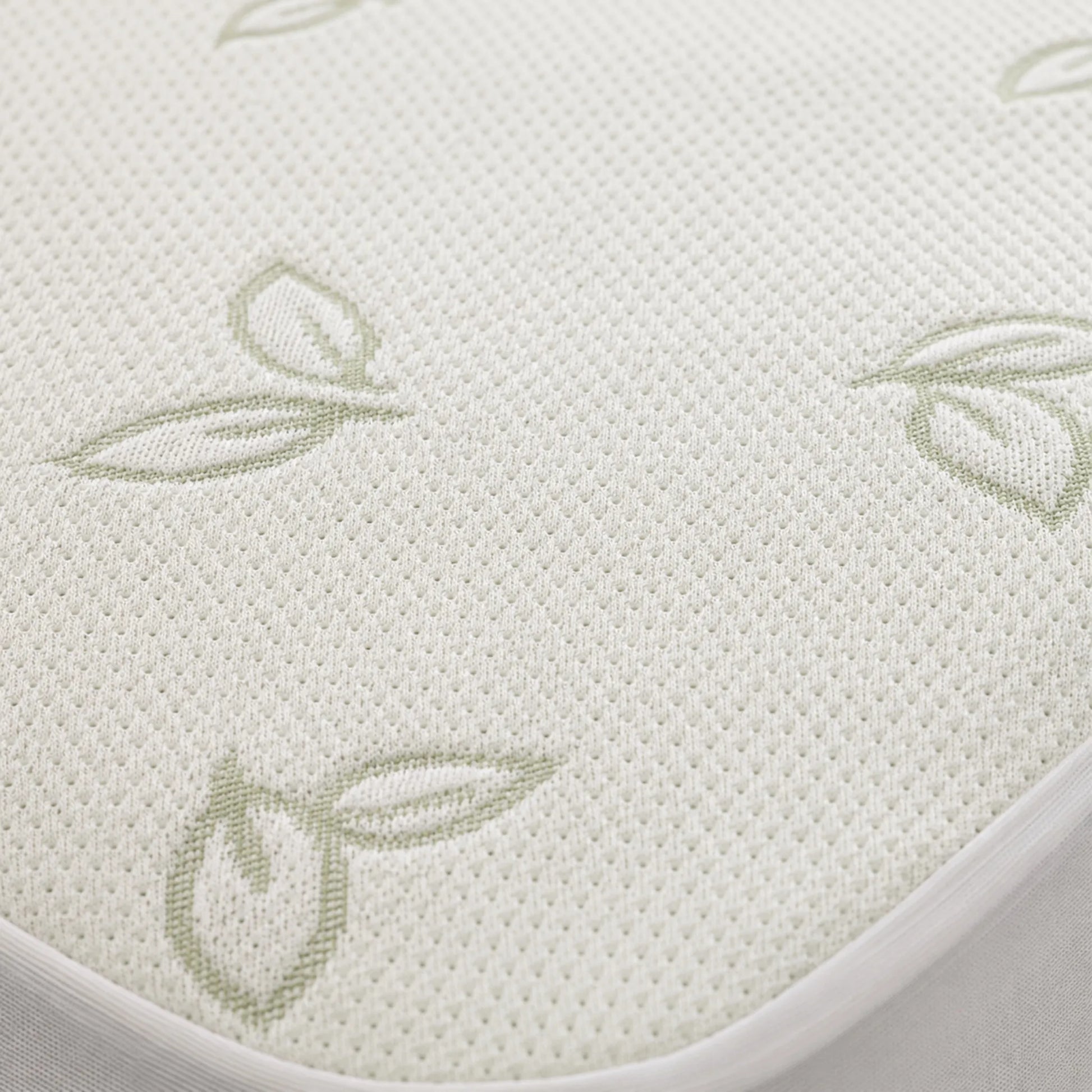 Primer plano de la textura blanca transpirable del protector de colchón Pacific Home con diseño tejido de hojas en tono verde suave.