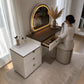 Tocador Vanity DT-1004 con espejo LED encendido en luz cálida, banco acolchado y gaveta abierta para maquillaje en habitación moderna.