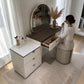Tocador Vanity DT-1004 con gaveta central abierta para organizar maquillaje, espejo LED y banco acolchado en color beige.