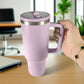 Vaso térmico de acero inoxidable color morado lila de 1200 ml con tapa y asa, sostenido en mano sobre escritorio de oficina.