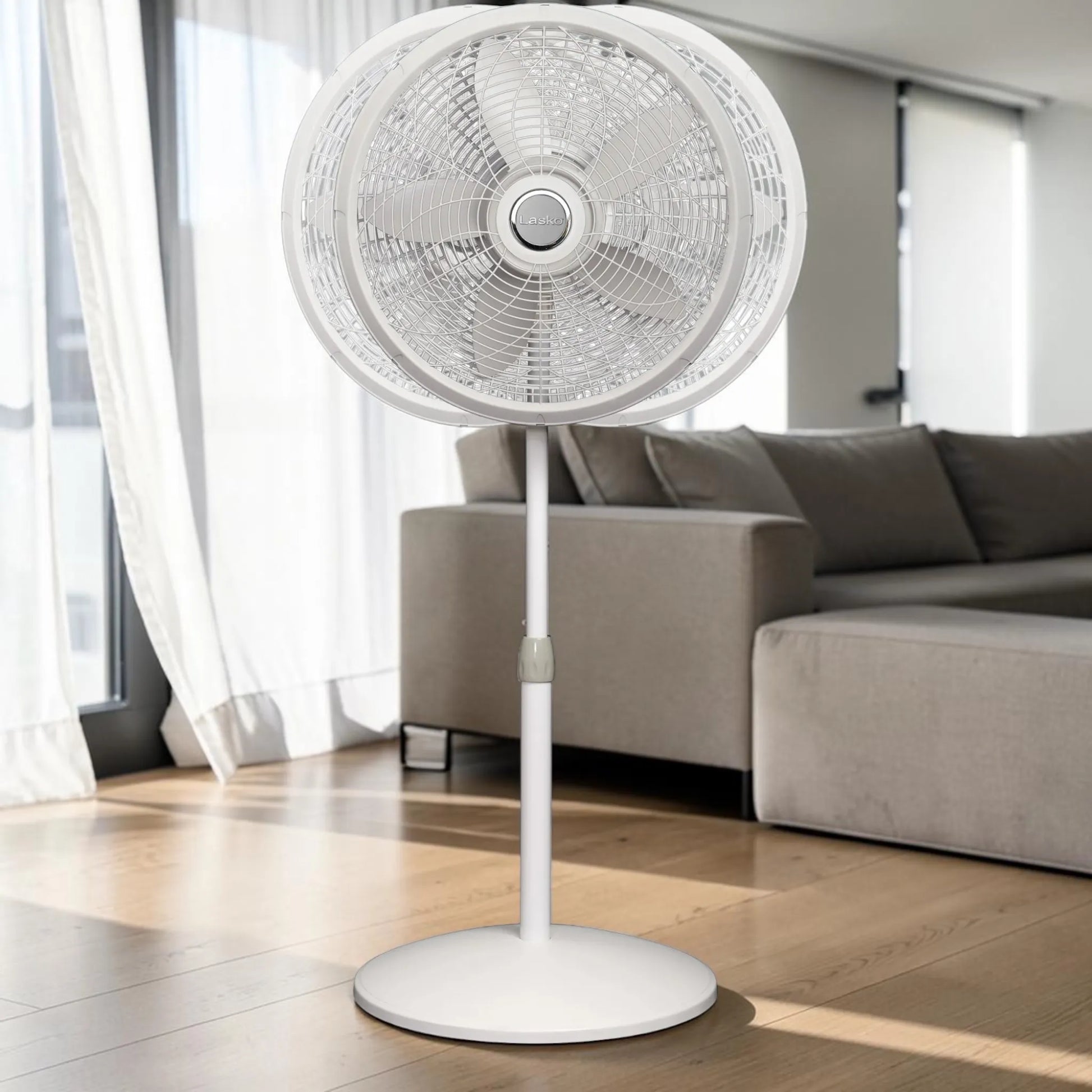 Ventilador pedestal Lasko 1820 blanco en sala moderna, vista frontal con rejilla circular y 5 aspas.