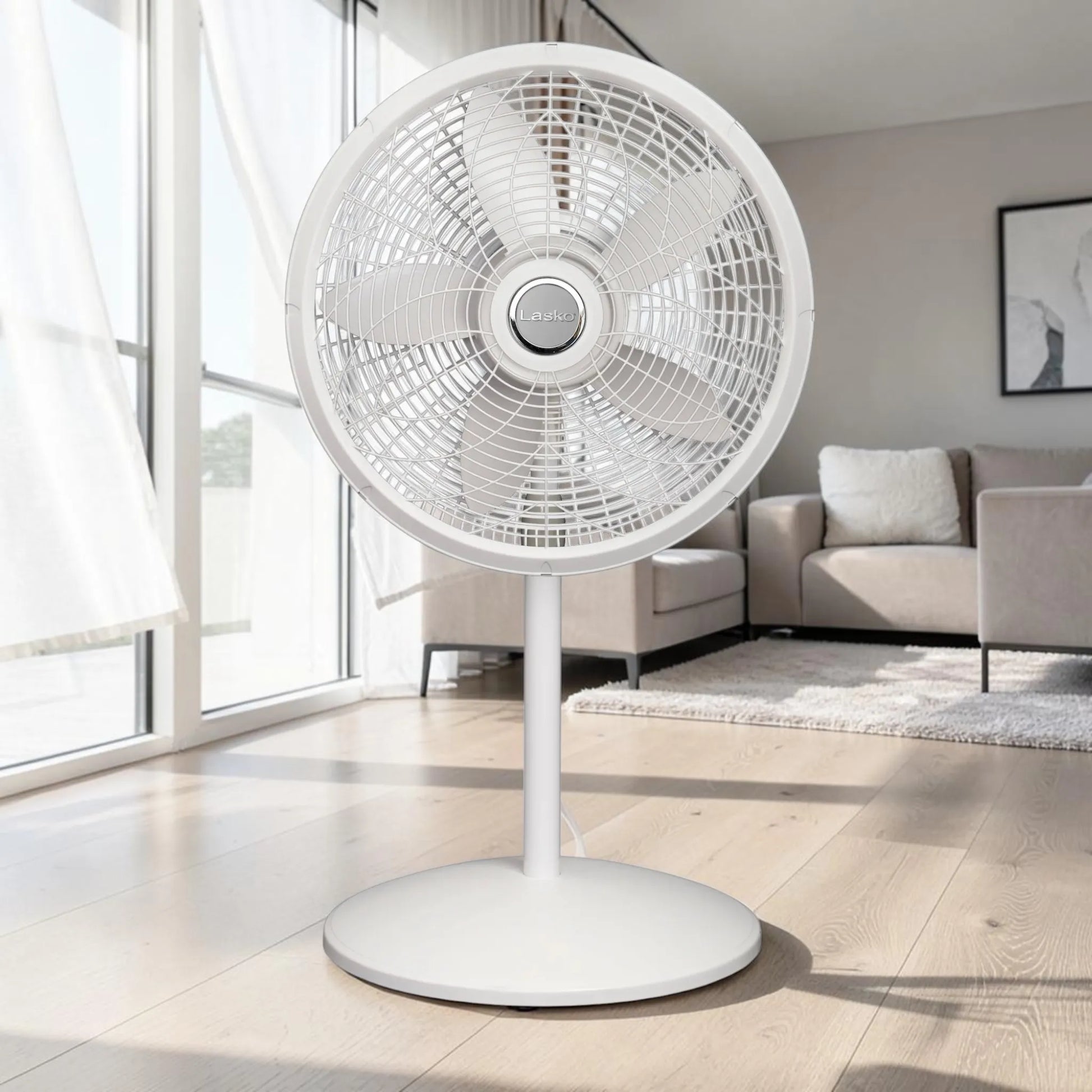 Ventilador pedestal Lasko 1820 blanco en sala iluminada, vista frontal con base redonda y rejilla protectora.
